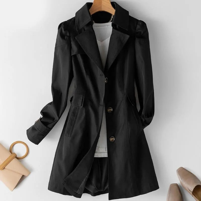 Black belted-waist trench coat with notch collar, shown buttoned over a white top on a hanger