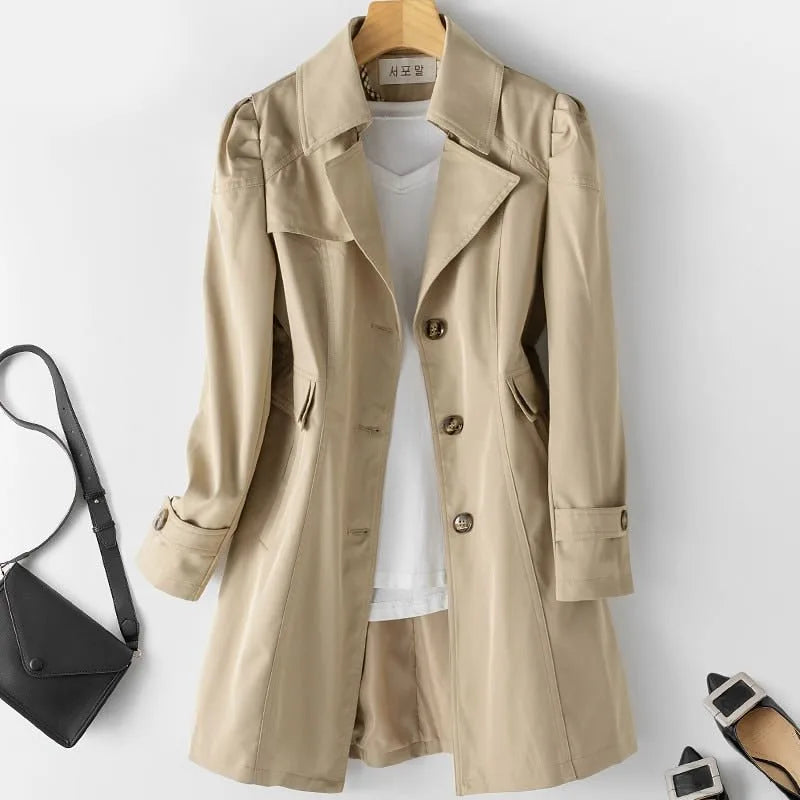 Khaki trench coat with puffed shoulders, matching bag and heels placed beside it as styling accessories