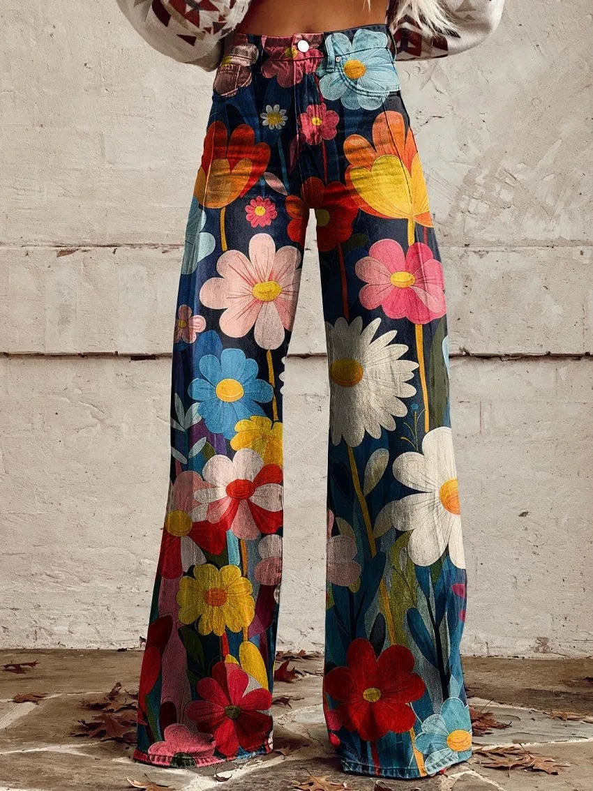 Rear view of high-waisted wide-leg denim trousers in a colourful daisy and floral print against a whitewashed brick wall
