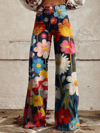 Rear view of high-waisted wide-leg denim trousers in a colourful daisy and floral print against a whitewashed brick wall