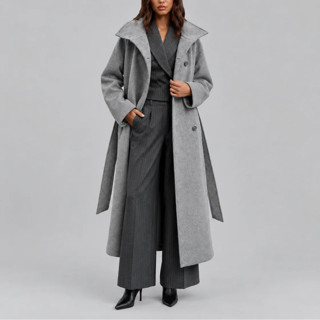 Grey belted longline coat worn open over a pinstripe waistcoat and wide-leg trousers